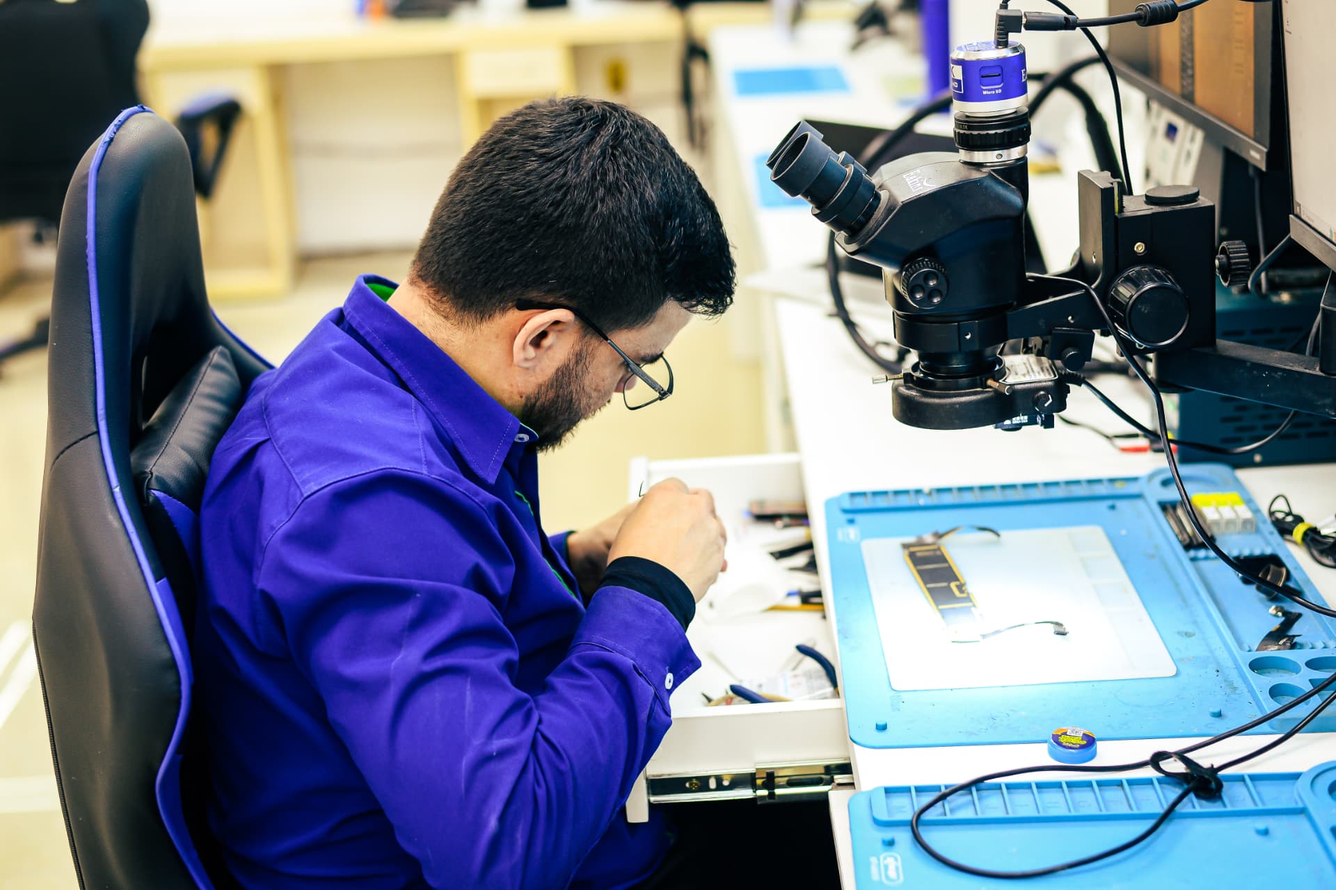Técnico MacFix reparando placa lógica de MacBook sob microscópio